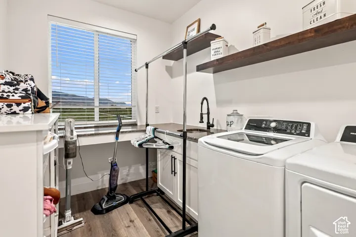 Laundry area with wood-finish flooring, white cabinetry, a built-in sink with a gooseneck faucet, and two dark wood floating shelves