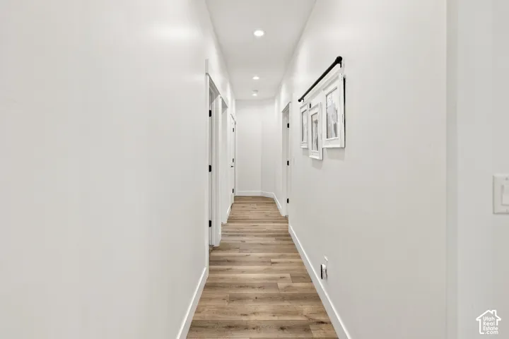 Hallway featuring wood-finish flooring, recessed lighting, and multiple doorways with dark hardware