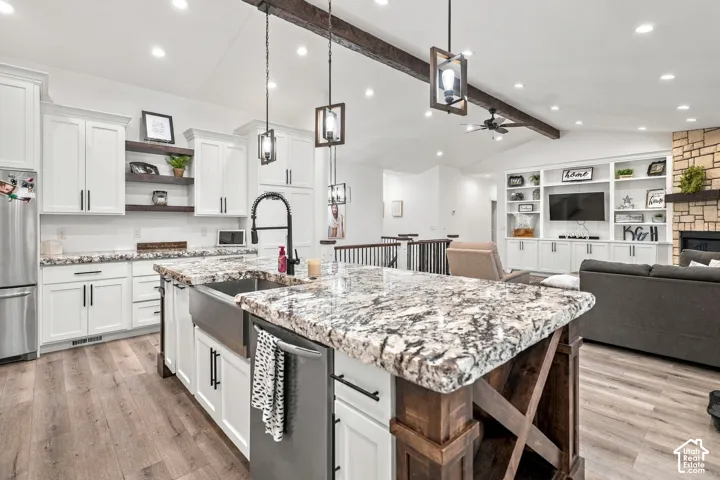 Chef's kitchen featuring white cabinetry with black hardware, a large center island with a decorative wood base and speckled stone countertop with undermount sink, stainless steel appliances, pendant lighting, recessed ceiling lights, and wood-finish floo