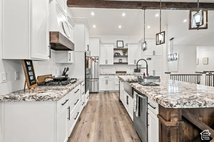 Spacious kitchen featuring white cabinetry, wood-finish flooring, a kitchen island with a farmhouse sink, stainless steel appliances, and pendant lighting