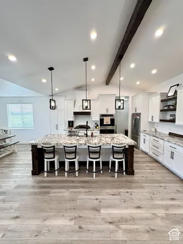 Kitchen featuring a large island with stone countertop, white cabinetry with dark hardware, wood-finish flooring, recessed lighting, and exposed ceiling beam