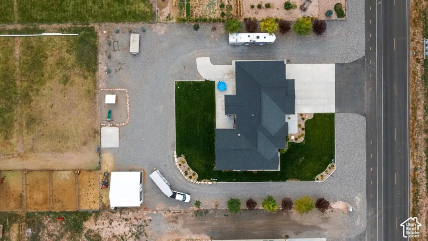 Gravel driveway surrounding a property with a dark roof, concrete paving, and landscaped lawn areas