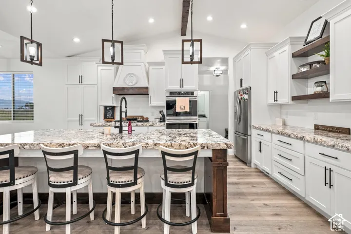 Spacious kitchen featuring an expansive center island with seating, white cabinetry, built-in stainless steel appliances, and wood-finish flooring