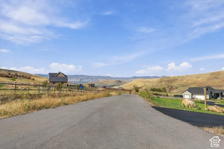 Paved roadway with expansive undeveloped land, bordered by wood fencing and a distant structure featuring a dark roof