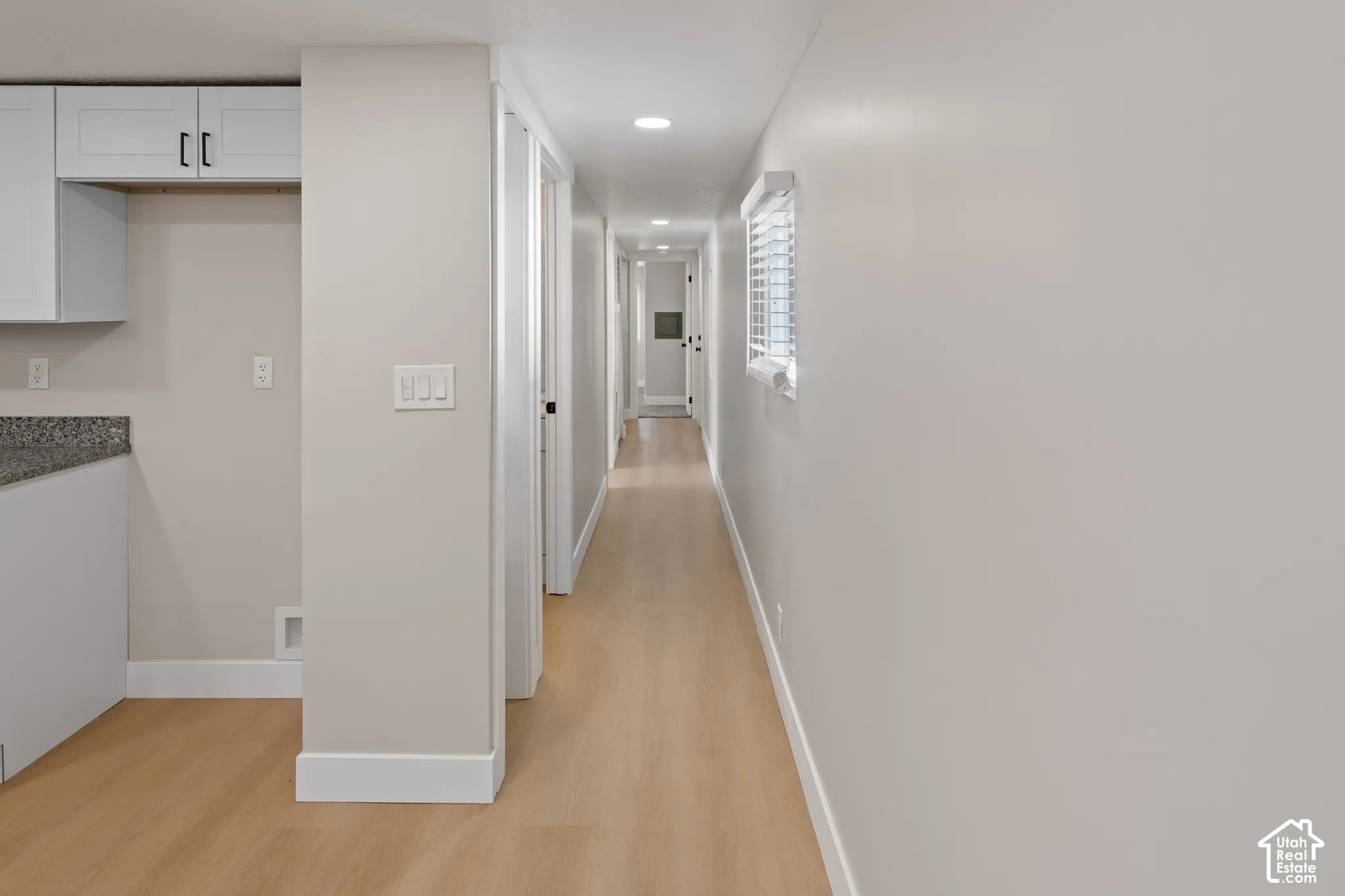Recessed lighting illuminating a hallway with wood-finish flooring, white trim, and a window with blinds