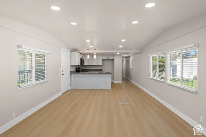 Open-concept living space featuring wood-finish flooring, recessed lighting, and a vaulted ceiling