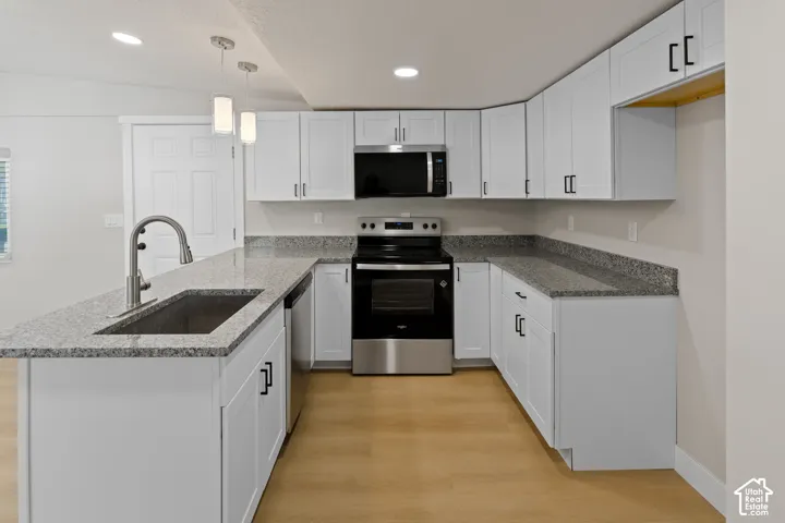 Modern kitchen with light wood-finish flooring, white cabinetry, dark hardware, and speckled countertops