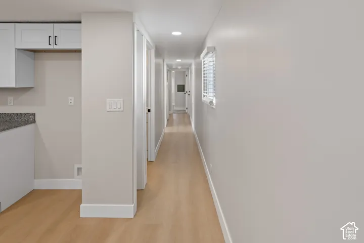 Recessed lighting illuminating a hallway with wood-finish flooring, white trim, and a window with blinds