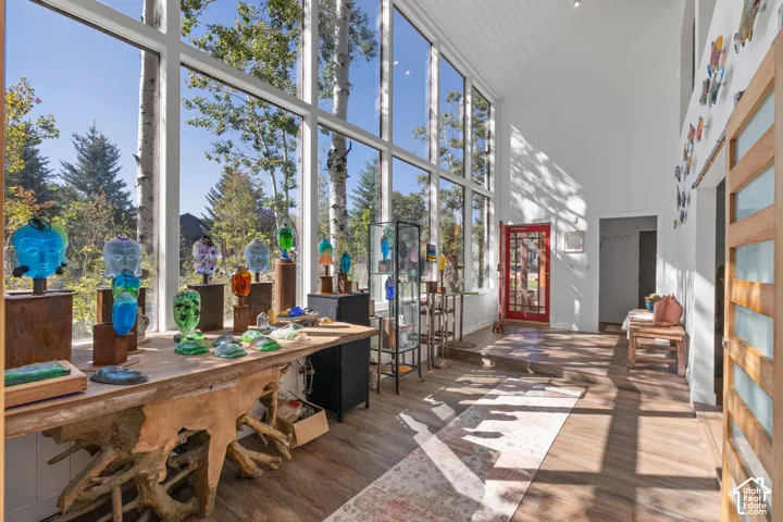 Vaulted ceiling with exposed beams, wood-finish flooring, full-height windows, a red entry door, and a sliding wood-panel door