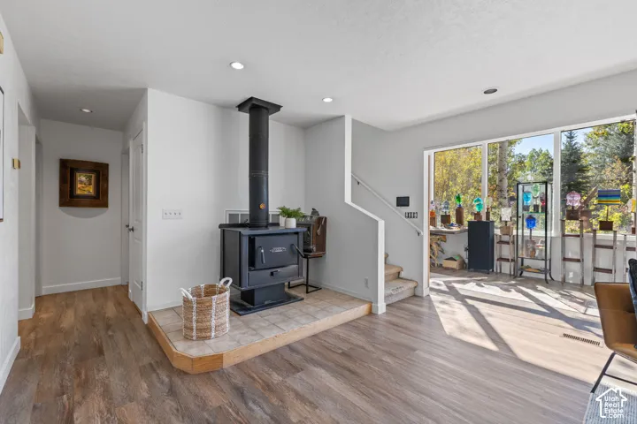 Wood-finish flooring, recessed lighting, and a black wood-burning stove with a tiled hearth
