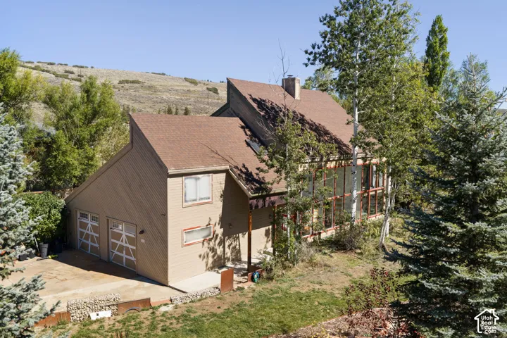 Multi-level residence featuring a two-car garage, multiple windows, and a brown shingle roof