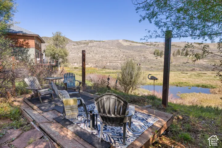 Outdoor seating area featuring a wood plank platform, a small body of water, and distant hills