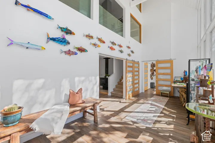 High ceilings with exposed beams, wood-finish flooring, and multiple windows