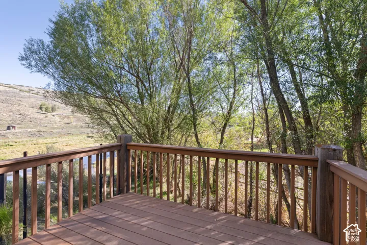 Expansive outdoor deck with wood-finish flooring and a wood railing, offering a natural setting with mature trees and a distant hillside