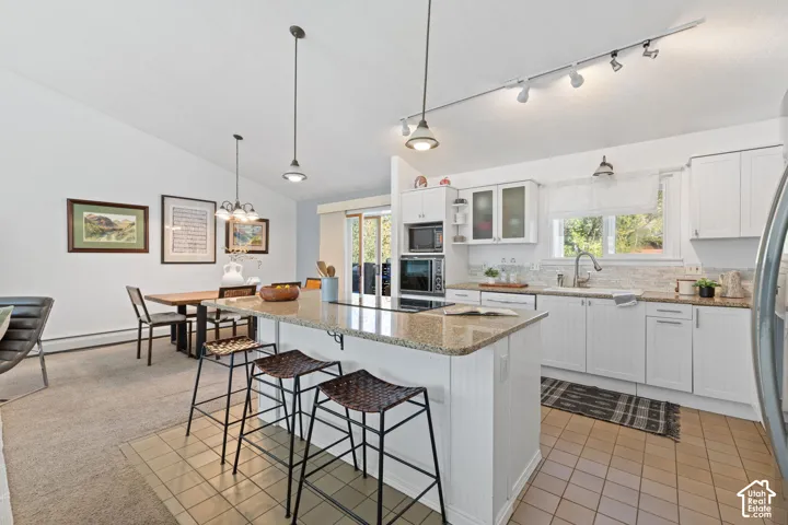 Kitchen featuring an island with a stone countertop, white cabinetry, integrated appliances, and track lighting