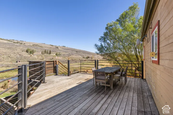Expansive outdoor deck with wood-plank flooring and metal railings, featuring a distant hilly landscape