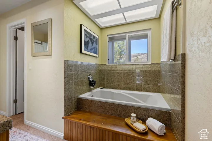 Built-in bathtub with tile surround, wood-paneled base, and large window