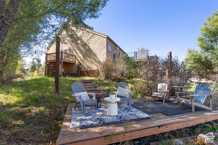 Expansive outdoor deck featuring a patterned area rug, a built-in balcony, and natural wood exterior siding