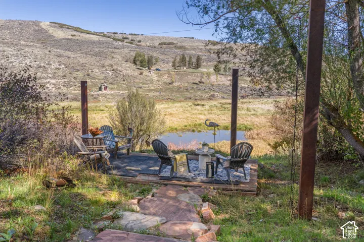 Outdoor platform patio with a small pond, surrounded by natural landscaping, and backed by a sloped terrain