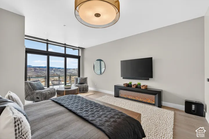 Expansive glass doors opening to a balcony, a linear electric fireplace, recessed lighting, a modern ceiling light fixture, and wood-finish flooring