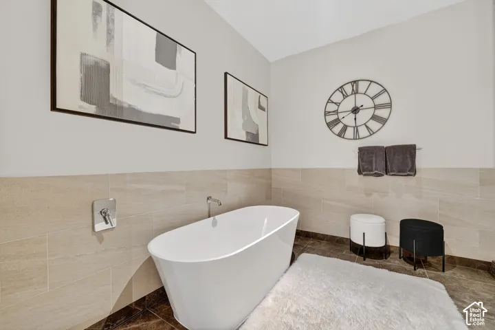 Freestanding white soaking tub with wall-mounted fixtures, accented by light-toned tiled wainscoting and dark floor tiles