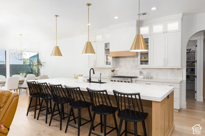 Spacious kitchen island with a light-toned countertop, brass pendant lighting, white cabinetry, integrated range, and light wood-finish flooring