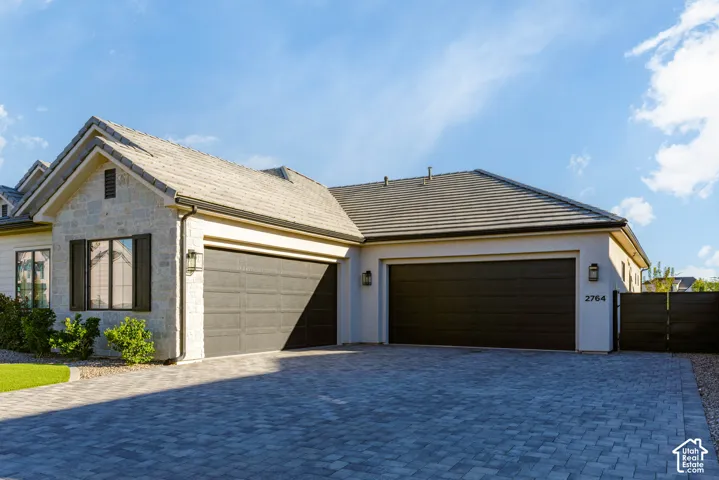 Paver driveway and walkway, stone and stucco exterior, dark panel garage doors, and exterior wall sconces