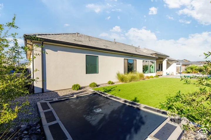 Expansive artificial turf lawn, stucco exterior, gray tile roofing, large dark-framed windows, and an in-ground trampoline