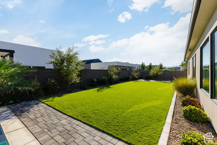 Expansive backyard featuring a lush green lawn, paver patio, established landscaping, and a perimeter wall