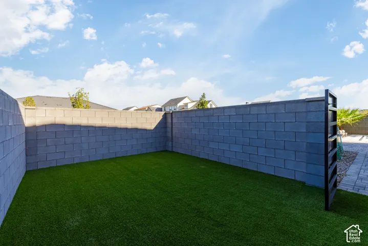 Enclosed backyard featuring artificial turf and block wall fencing