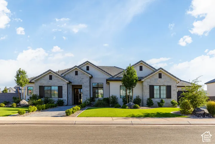 Contemporary exterior with stone facade accents, dark framed windows, a dark shingle roof, landscaped front yard with a manicured lawn, and a paver driveway