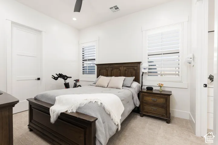 Recessed lighting, wood-finish bed frame, wood-finish nightstand, white plantation shutters, and a ceiling fan