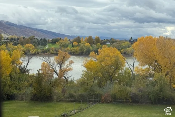 Expansive manicured lawn with a wire fence, backed by a body of water, and surrounded by mature trees with vibrant foliage