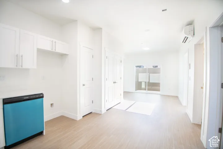 Light wood-finish flooring throughout, white shaker-style cabinetry, and a built-in dishwasher