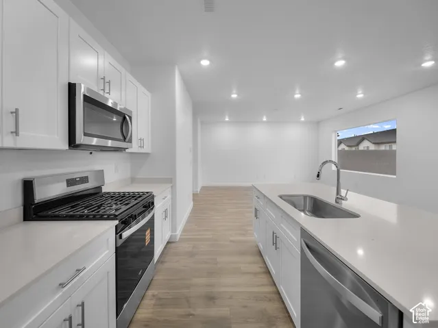 Kitchen featuring white cabinetry, stainless steel appliances, light-toned countertops, and wood-finish flooring