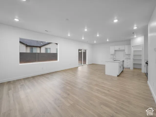 Open-concept living space with wood-finish flooring, recessed lighting, and a kitchen featuring white cabinetry, an island with an undermount sink, and a sliding glass door