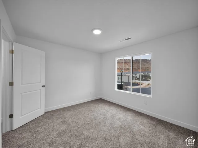 Recessed ceiling lighting, white interior door, light-colored walls, broad window, and gray carpeted flooring