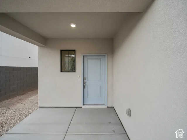Covered entryway with recessed lighting, stucco exterior, light blue panel door, and concrete pad