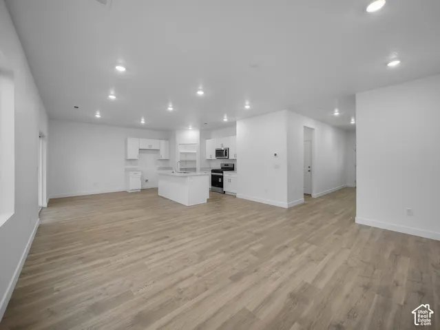 Open-concept living space featuring wood-finish flooring, recessed lighting, white cabinetry, and stainless steel appliances