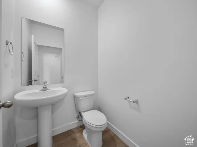 Pedestal sink with chrome faucet, wall-mounted mirror, and wood-finish flooring
