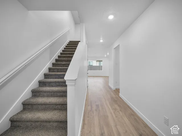 Carpeted staircase with white handrail, wood-finish flooring, recessed lighting, and white walls