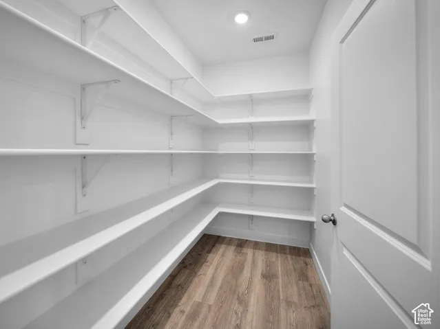 Walk-in pantry with extensive white shelving, wood-finish flooring, and recessed ceiling lighting