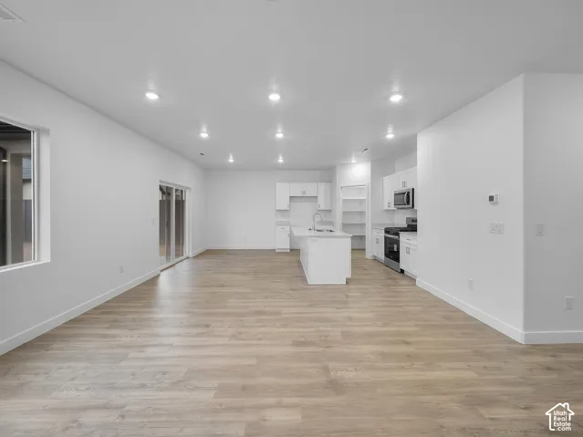 Open-concept living space featuring wood-finish flooring, recessed lighting, and a white kitchen with an island