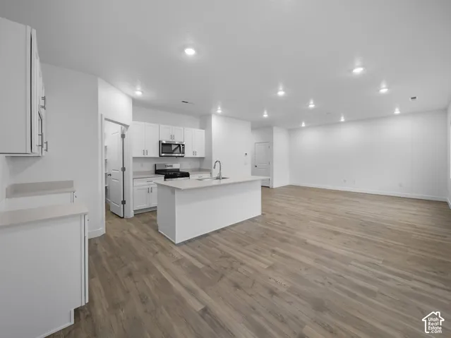 Kitchen featuring white cabinetry, light-colored countertops, stainless steel appliances, and a central island with a sink