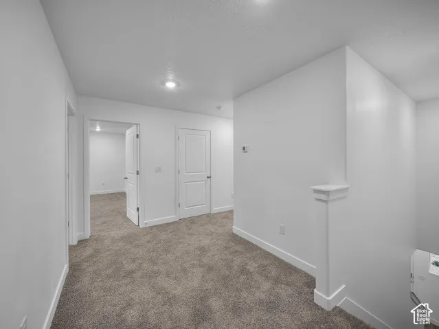Recessed lighting illuminates the carpeted hallway with painted walls, featuring a half-wall banister