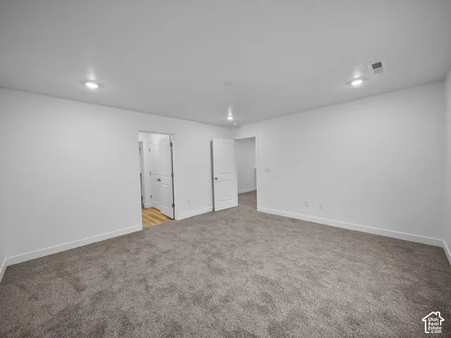 Recessed lighting, neutral paint, gray carpet, white trim, and a white interior door