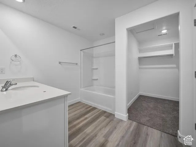 Bathroom featuring a white vanity with an integrated sink and chrome faucet, a white bathtub with a shower, and wood-finish flooring
