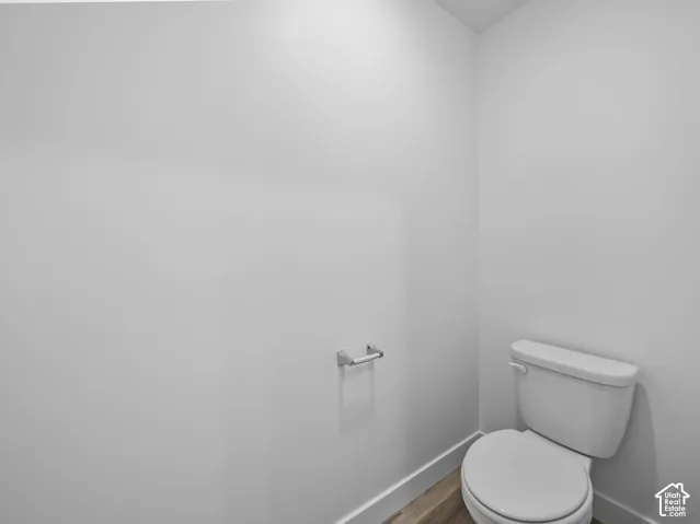 White walls with wood-finish flooring and white baseboards, featuring a white toilet and a chrome toilet paper holder