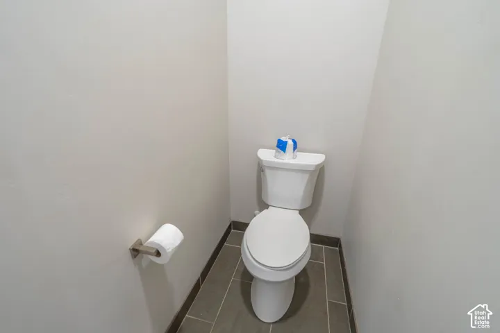 White two-piece toilet with a closed-front seat, set against light neutral walls, and featuring large format gray floor tiles