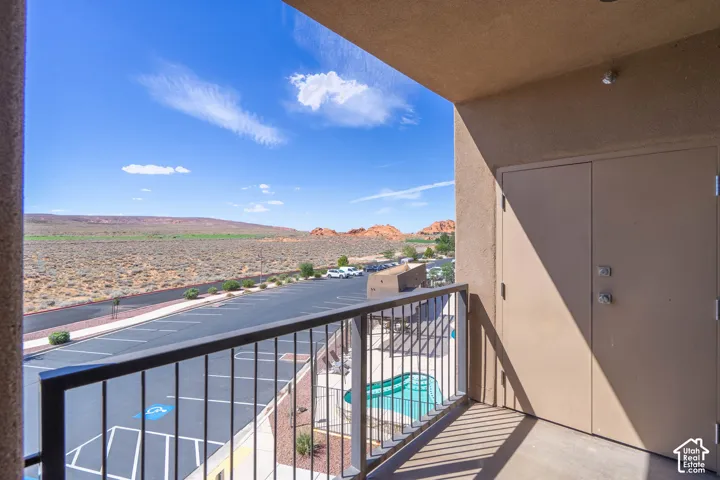 Covered balcony with black metal railing, offering expansive desert scenery and a partial view of the outdoor pool
